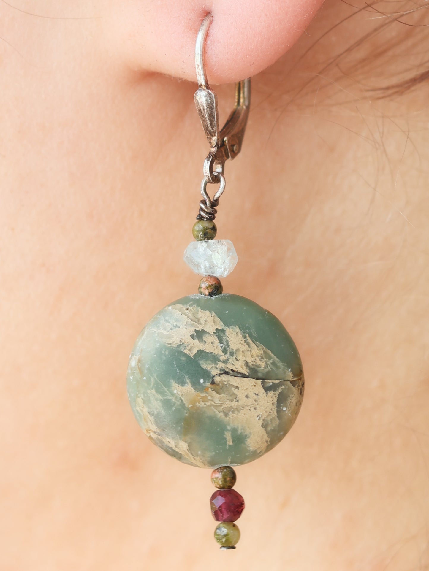 Close-up of a green marbled bead earring with smaller beads on a person's ear.