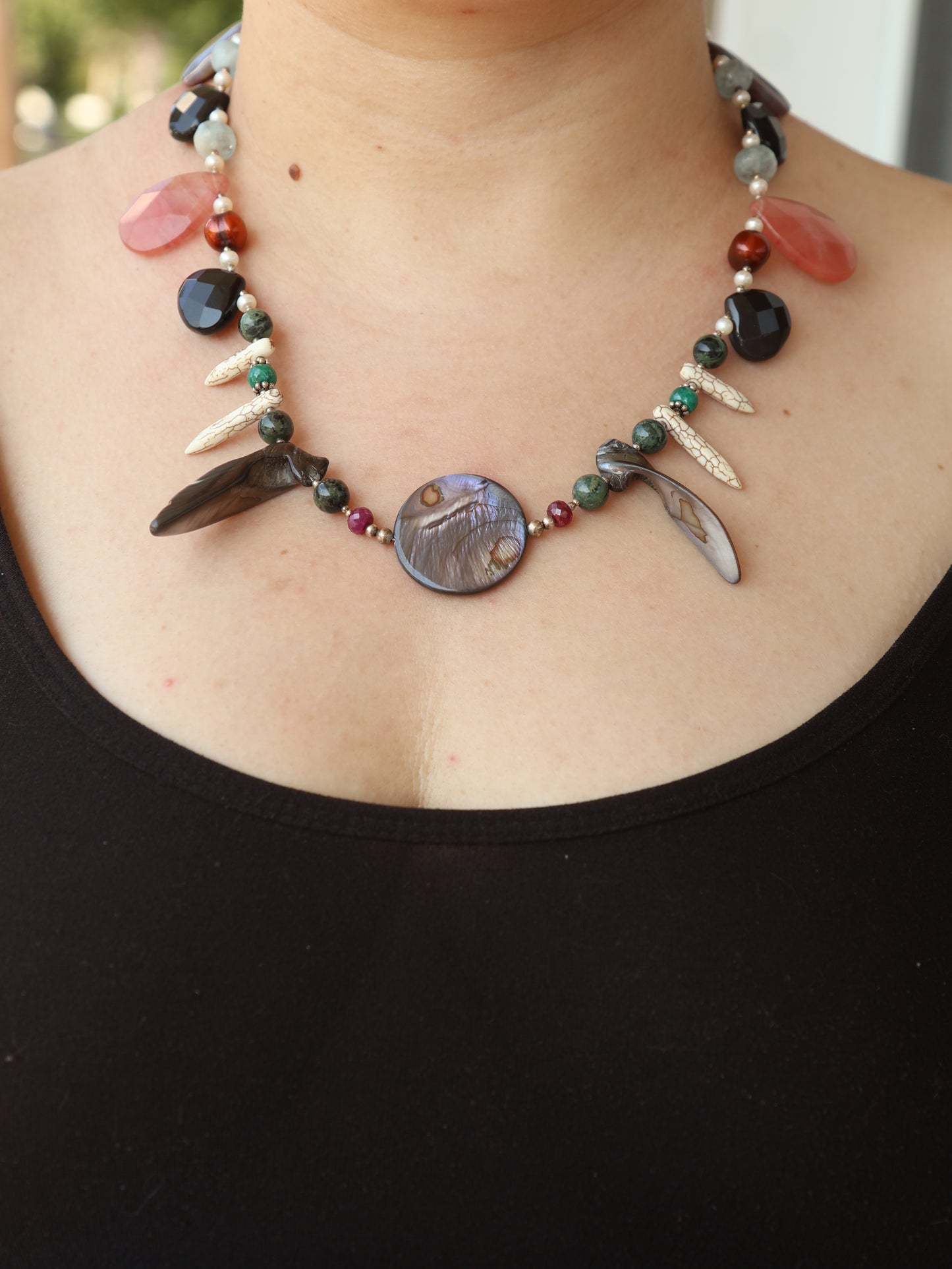 Necklace with various beads and a large central stone on a person's neck.