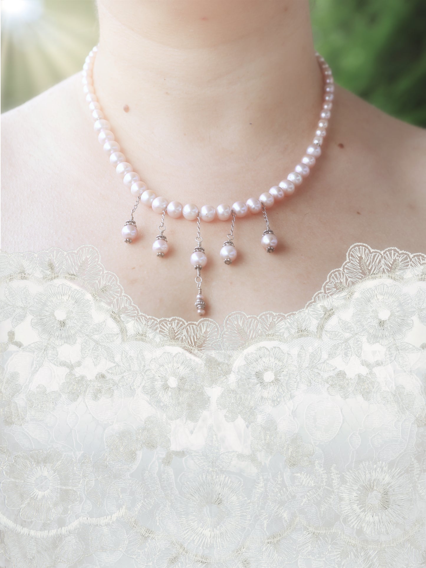 Soft pink pearl necklace with five pearl droplets dangling from silver chain on a person wearing a white lace wedding dress.