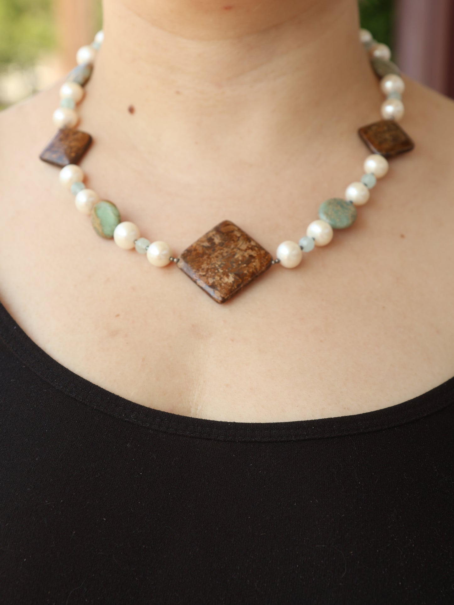 Necklace with brown and green beads on a person wearing a black top.