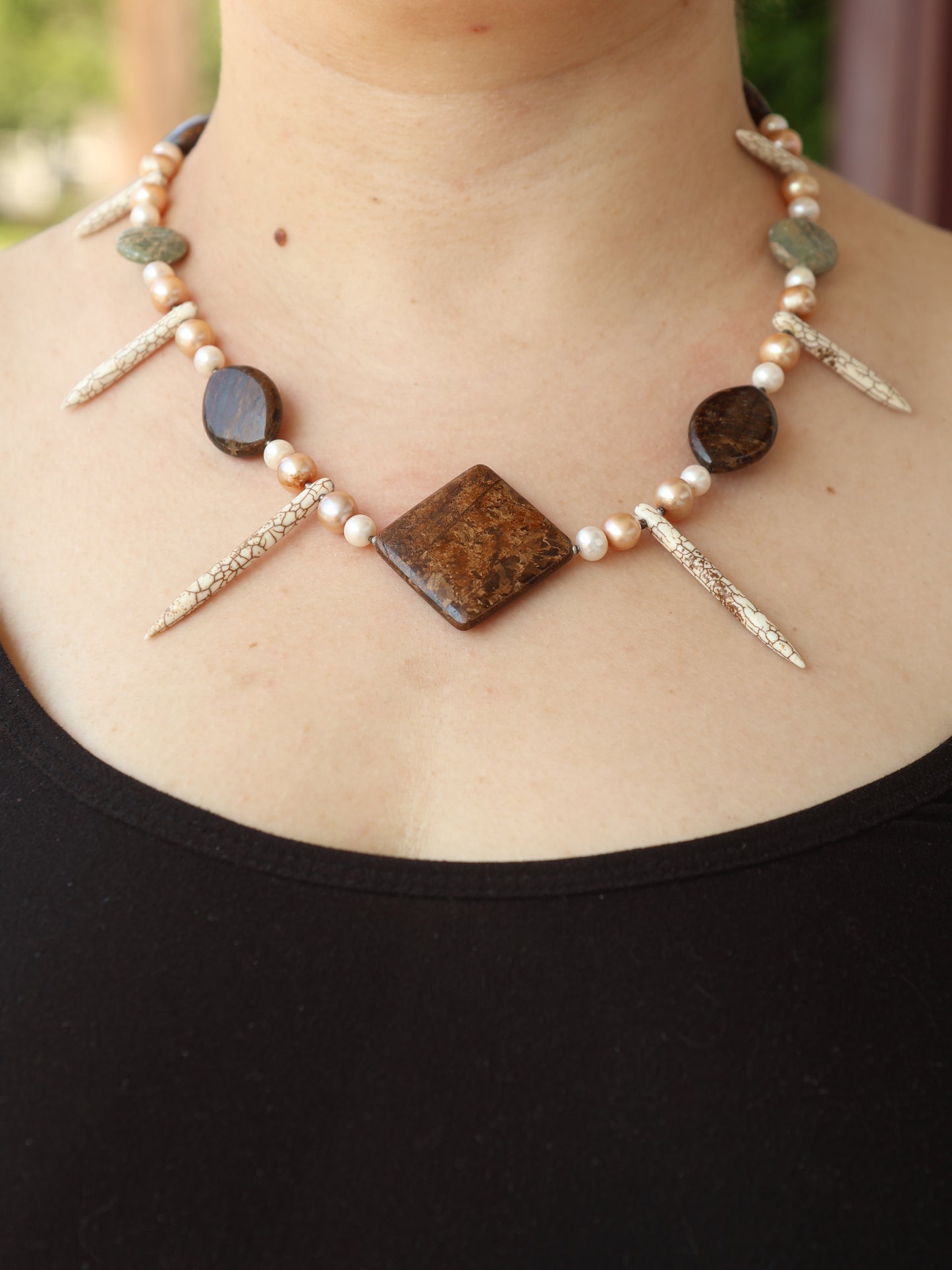 Necklace with stones and pearls on a person wearing a black top.