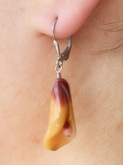 Amber-colored calla lily earring on a person's ear with a close-up view.