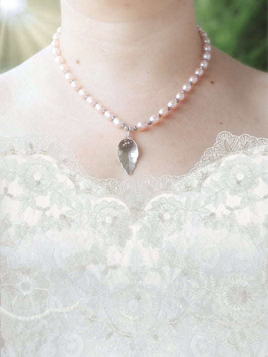 Soft pink, pearl necklace with a silver calla lily pendant on a white lace wedding dress against a blurred green background