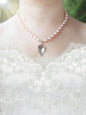 Soft pink, pearl necklace with a silver calla lily pendant on a white lace wedding dress against a blurred green background