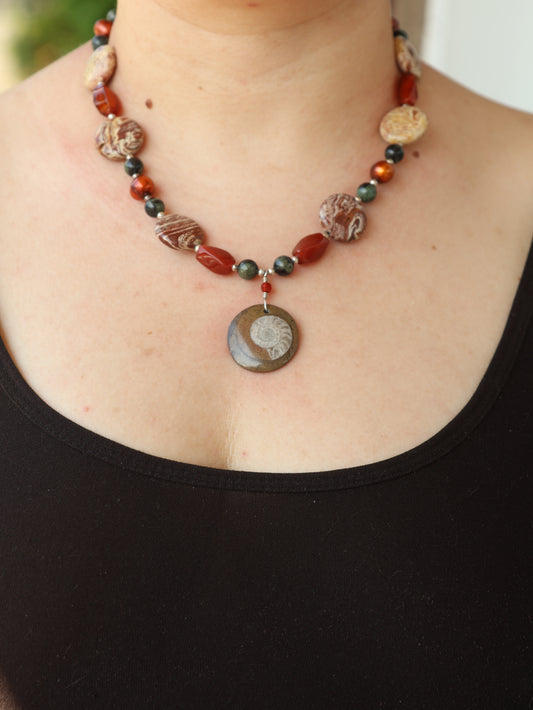 Necklace with beads and a circular pendant on a person's neck against a black background