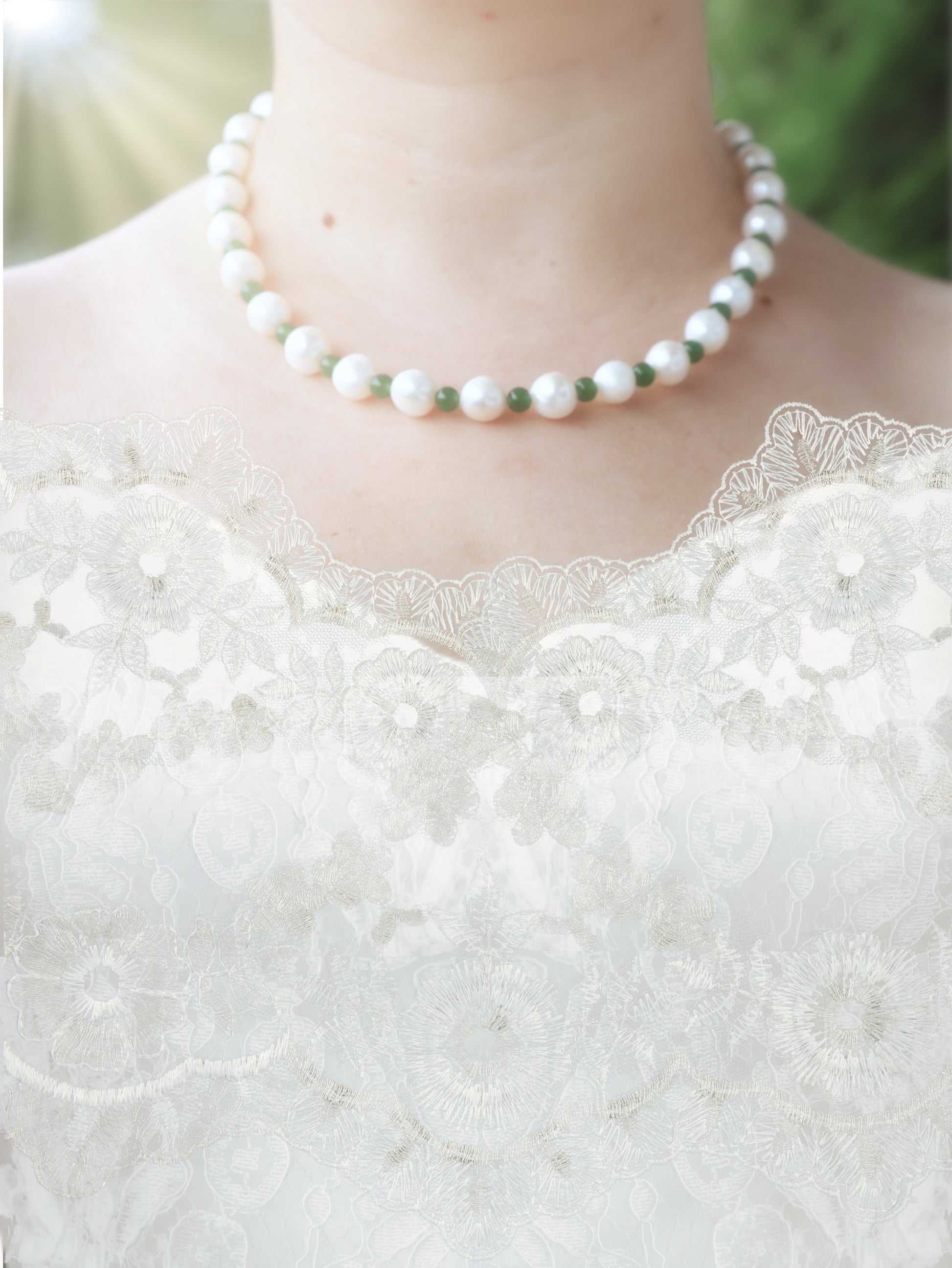 Pearl necklace with each pearl separated by small, round emerald beads - worn by a person in a white lace wedding dress with a blurred green background
