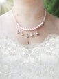 Soft pink pearl necklace with five pearl droplets dangling from silver chain on a person wearing a white lace wedding dress.