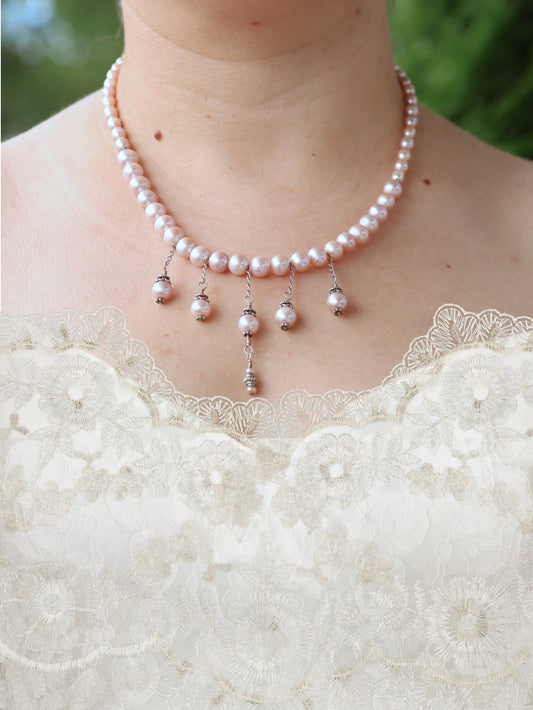 Pearl necklace with dangling beads worn by a person in a white lace garment.