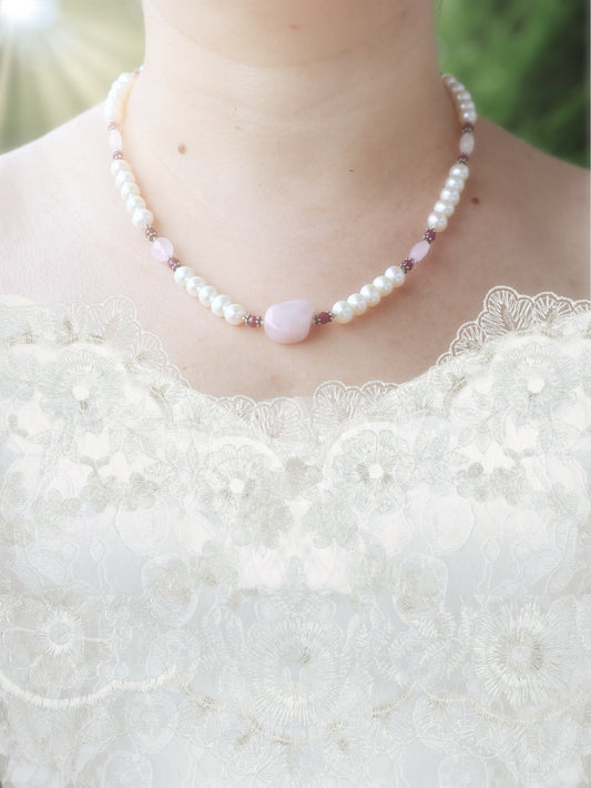 Pearl necklace with pink rose quartz, and small ruby accents worn by a person in a white lace wedding dress.