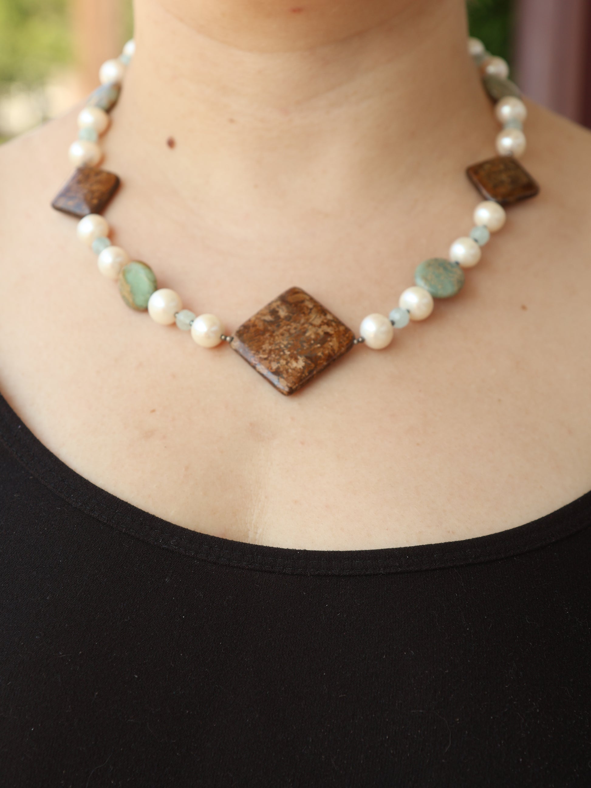 Necklace with brown and green beads on a person wearing a black top.